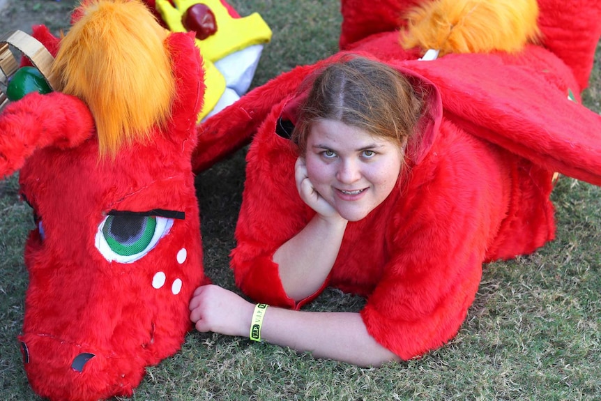 A woman wearing a furry red horse suit reclines on the ground