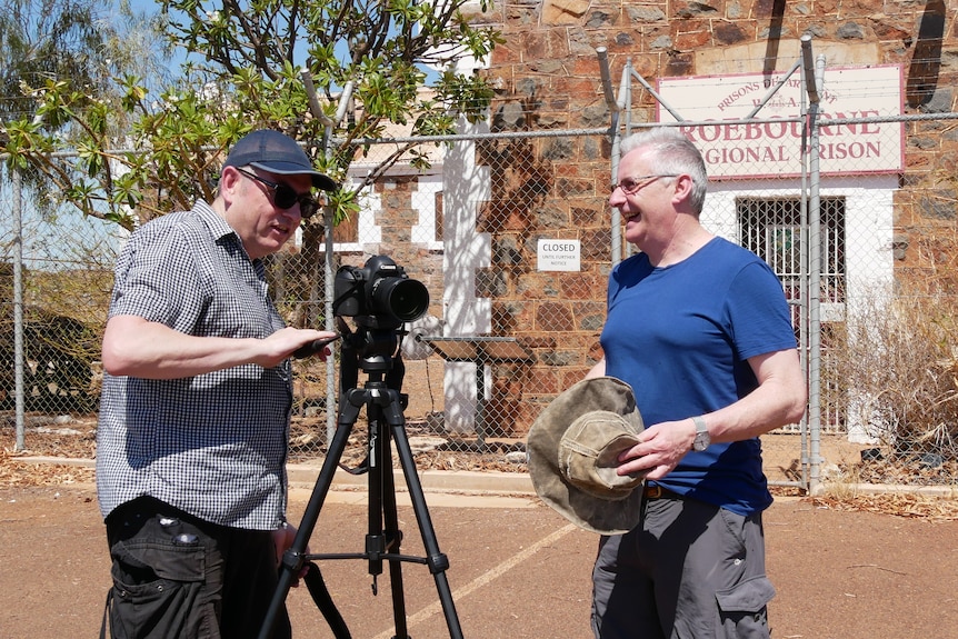 Two men stand outside old Roebourne Regional Prison with a camera on a tripod