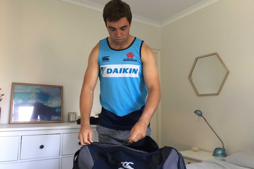 A young man in his bedroom packing his bag before rugby training.