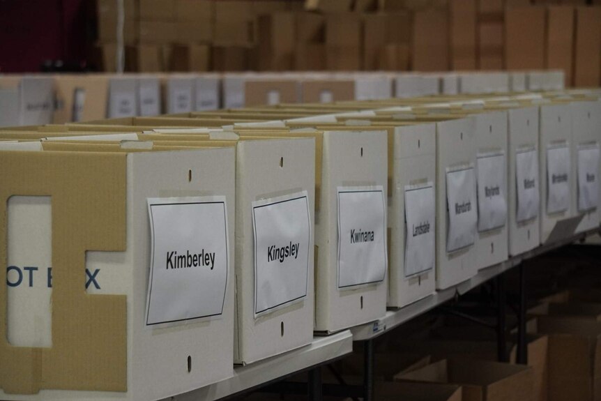 A row of boxes with the names of WA electorates printed on paper taped to the front.