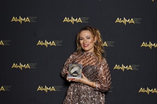 an image of Tania Doko in front of a AWMA media wall holding an award