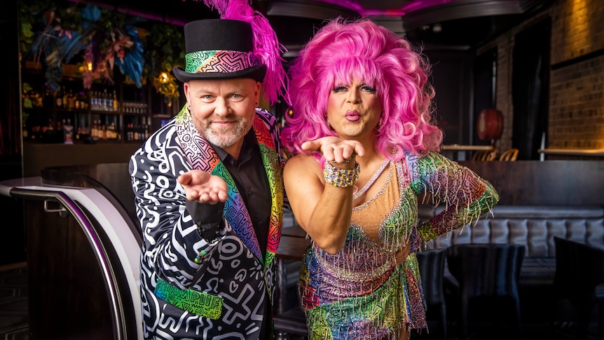 Two people dressed in colourful outfits blow kisses