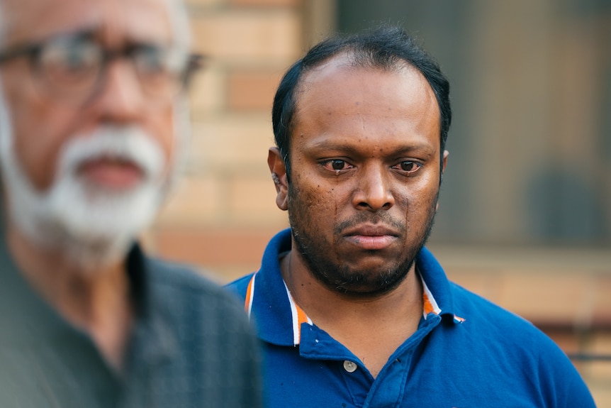 A close up of Aswath wearing a dark blue t-shirt, with tears streaming down his face.