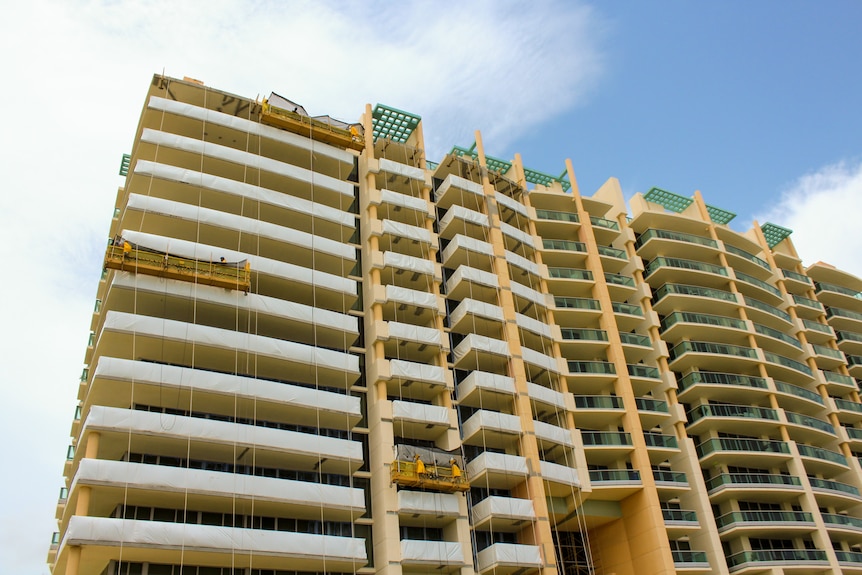 Half of a 20-story condo building is covered in construction gear as workers make repairs