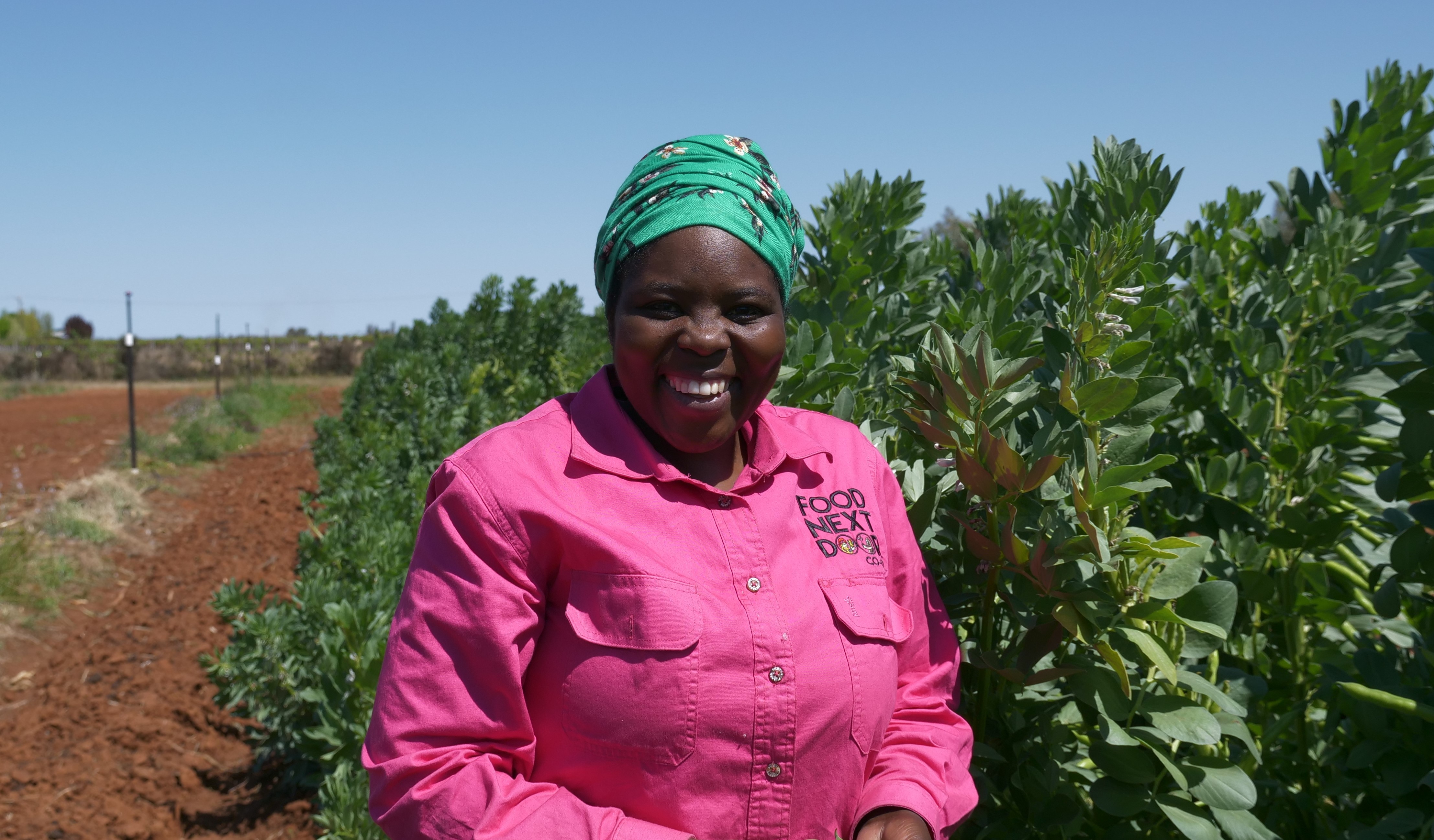 A Burundian woman standing in front of broad beans smiling.