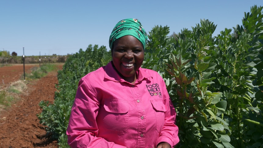 A Burundian woman standing in front of broad beans smiling.