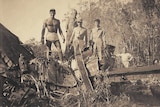 A black and white photo of five men standing on the wreckage of a plane crash