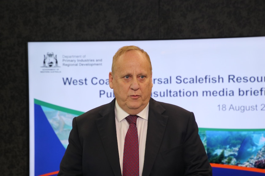 Man in suit jacket and tie looks out with projection of fishery discussion paper in background