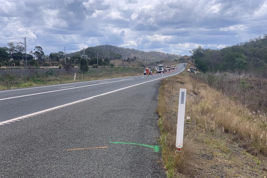 A stretch of road, roadworks trucks and cars in background. 