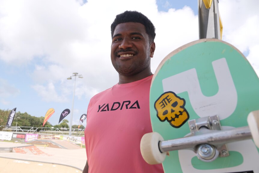Young fijian  man stands smiling with skateboard. 