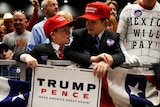 Children wearing "Make America Great Again" hats surrounded by supporters at a Donald Trump rally.