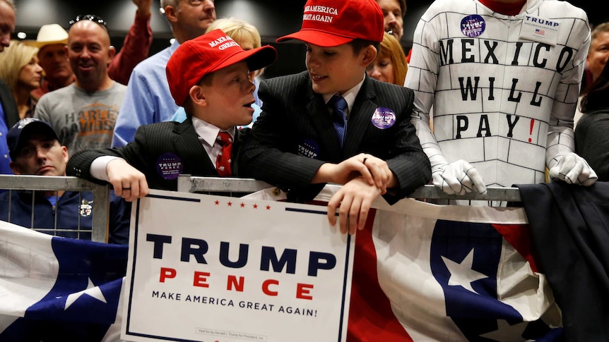 Children wearing "Make America Great Again" hats surrounded by supporters at a Donald Trump rally.