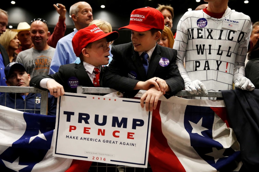 Children wearing "Make America Great Again" hats surrounded by supporters at a Donald Trump rally.