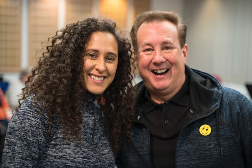 An woman with long curly brown hair and a man pose together, big smiles