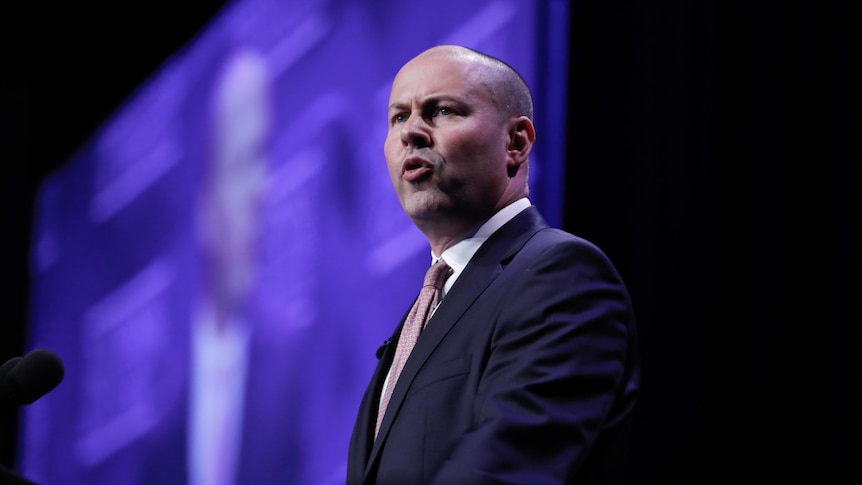 Josh Frydenberg speaks at a lecturn. A screen behind him shows his face