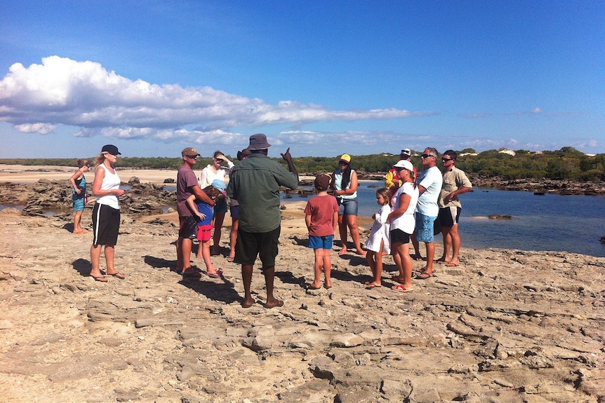 An Aboriginal man with a group of tourists, all standing on a piece of rocky coastline.