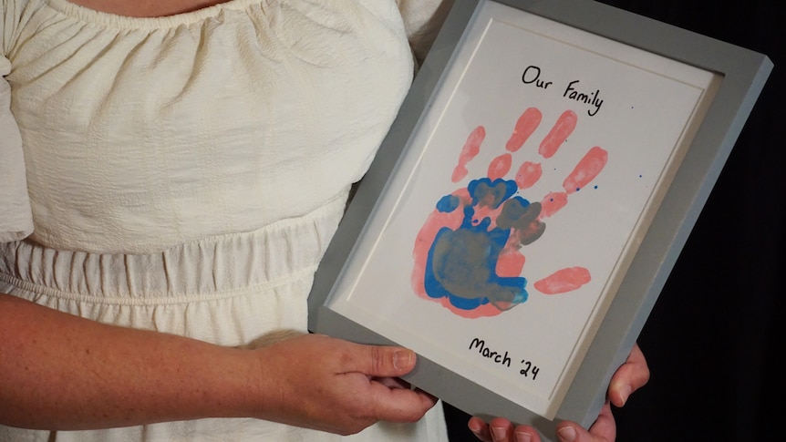 An unidentifiable photo of Edwina holding a handprint painting she did with her children.