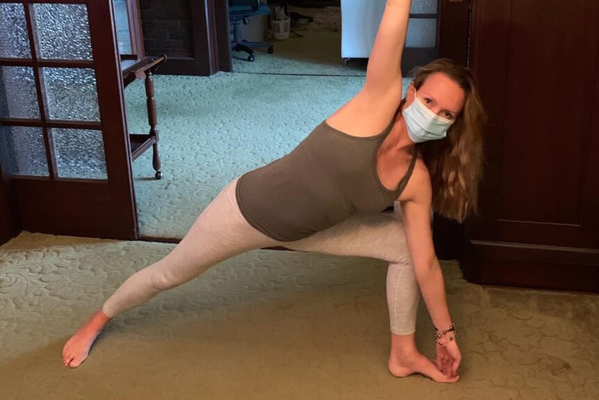 A woman stretching while wearing a face mask