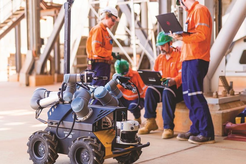 Workers on a mine site control a small, wheeled robot using a laptop