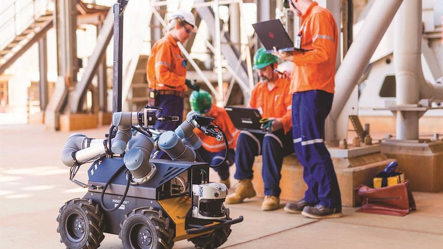 Workers on a mine site control a small, wheeled robot using a laptop