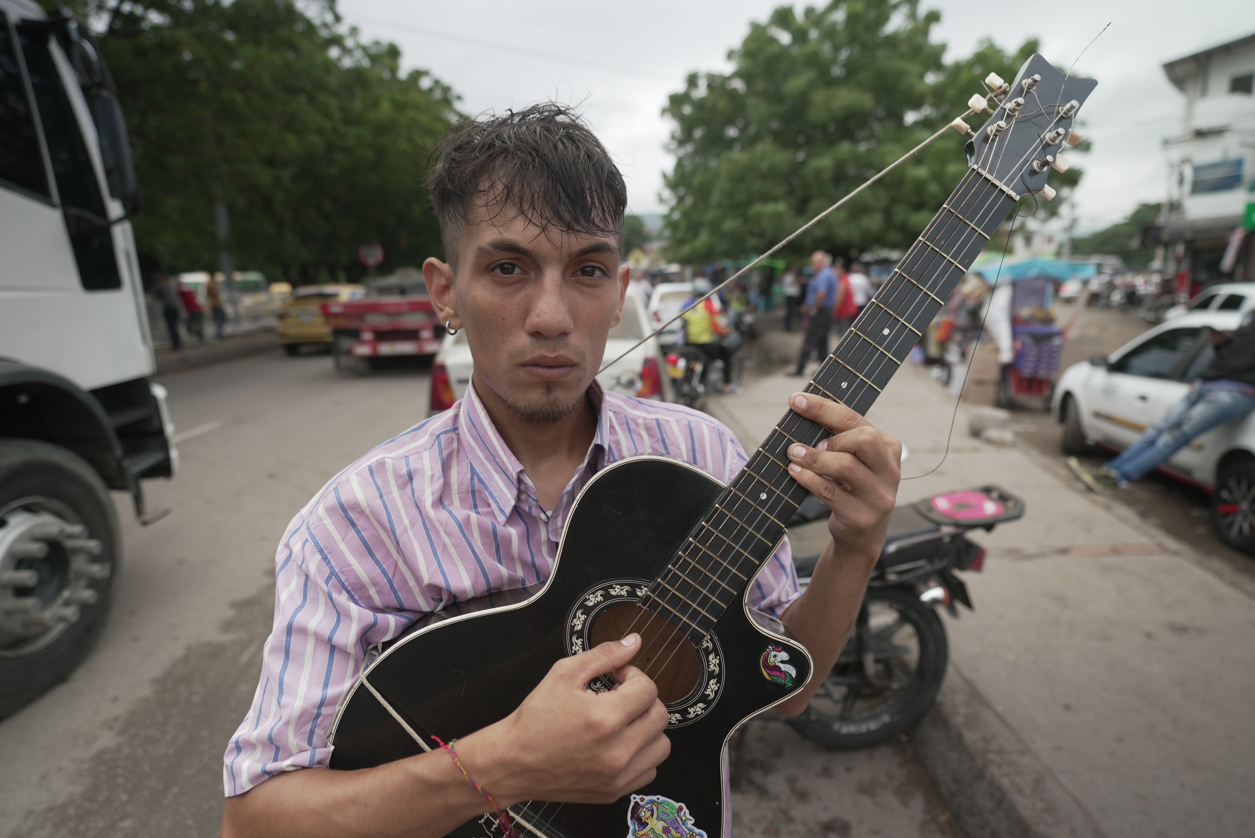 Um homem de camisa listrada segurando um violão preto. 