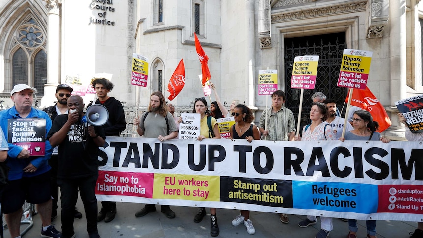 Protesters hold up placards saying "Oppose Tommy Robinson" and hold a banner saying "Stand up to racism".