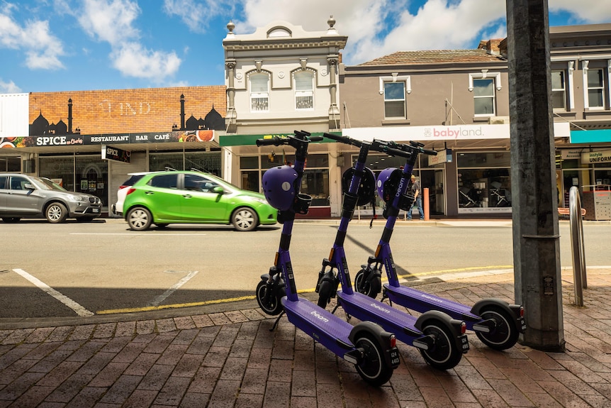 Three purple e-scooters parked on a footpath.
