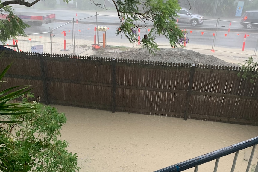 Muddy water covering grass behind a fence in a backyard.