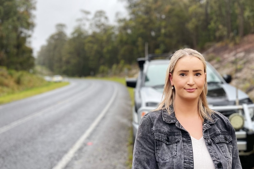 A women with blonde hair is standing on the side of the road near the car accident 