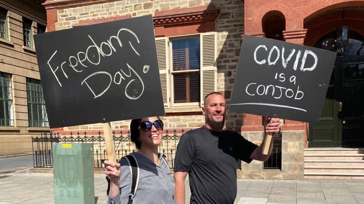 A woman and a man holding black protest signs while walking on a city street in front of a 19th century building