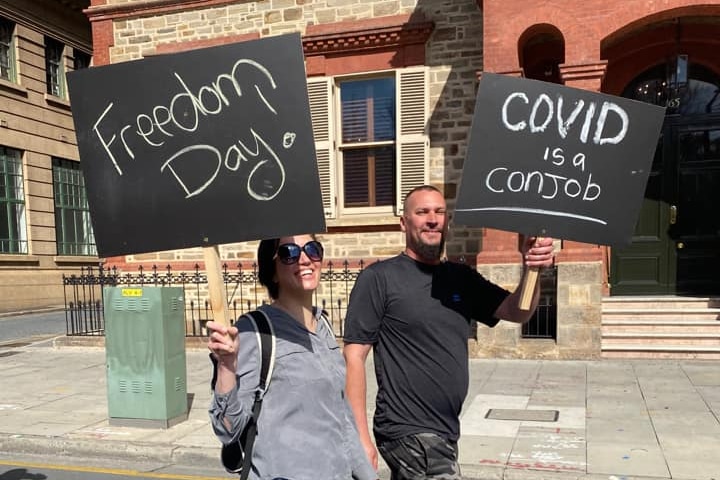 A woman and a man holding black protest signs while walking on a city street in front of a 19th century building