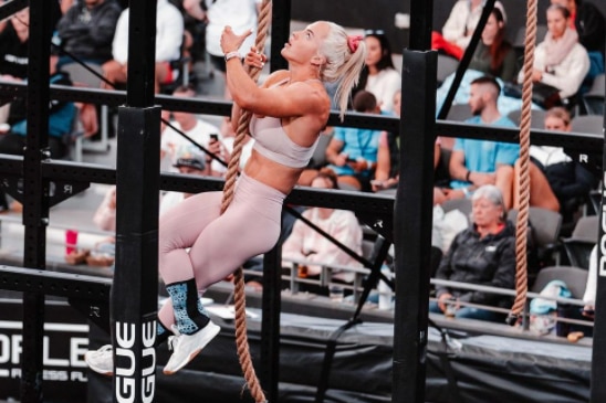 A well-muscled woman in pink exercise gears scrambles up a rope