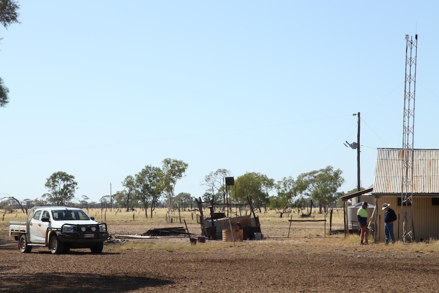 Two men stand beneath a tower on an outback station.