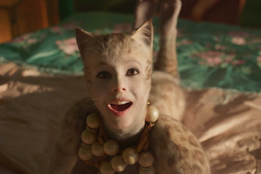 A cat with a human face and feet wearing a big necklace, lying on a bed and looking up in delight
