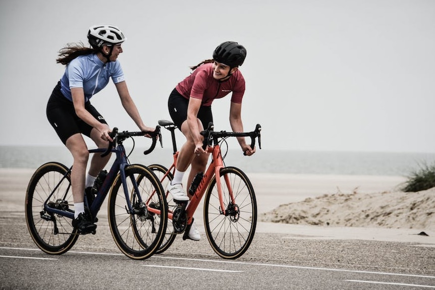 Two women riding bikes on an empty road