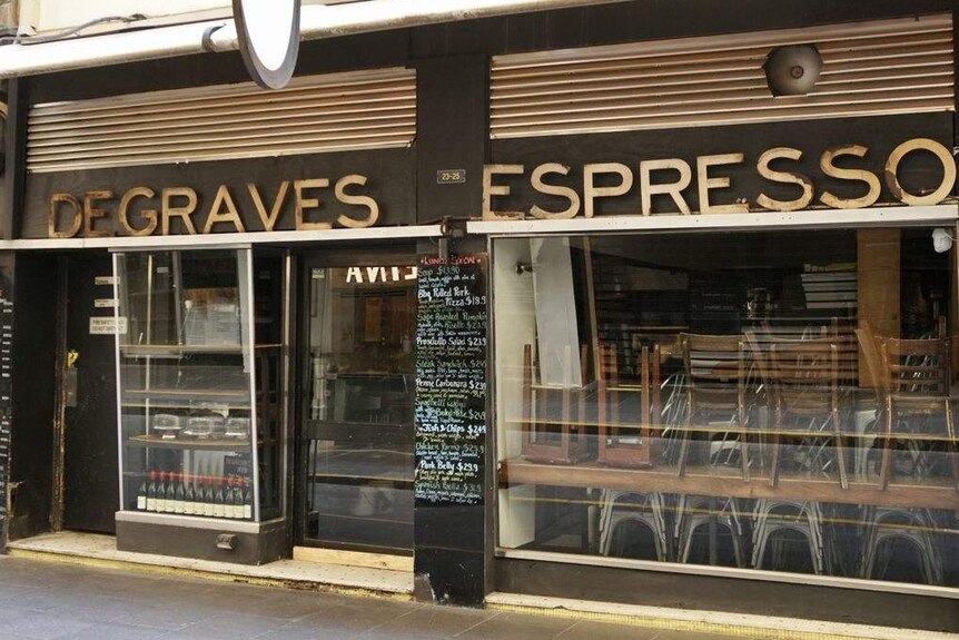 The outside of a closed cafe filled with stacked dining chairs, with 'Degraves Espresso' written on the side.