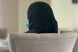 A woman who is wearing a black head covering sits in a chair. Her face is not visible.
