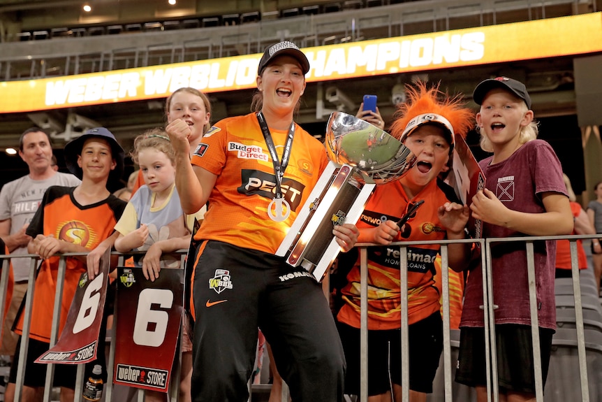 La jugadora de Perth Scorchers, Taneale Peschel, sostiene el trofeo WBBL con fanáticos