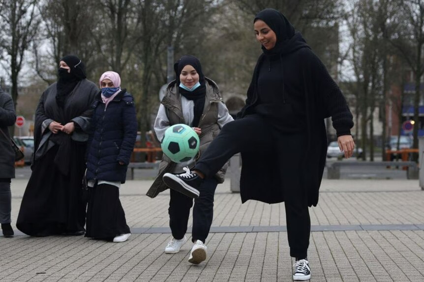 Women kicking around a bright green soccer ball
