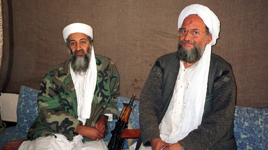 Osama bin Laden and Ayman al-Zawahiri in army fatigues sitting on the floor next to a rifle