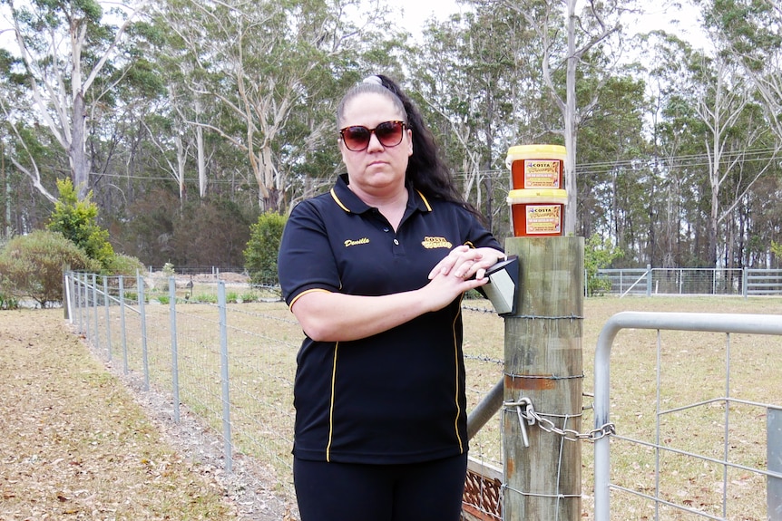 A woman wearing a black shirt leans on a fence post with two tubs of honey on top.
