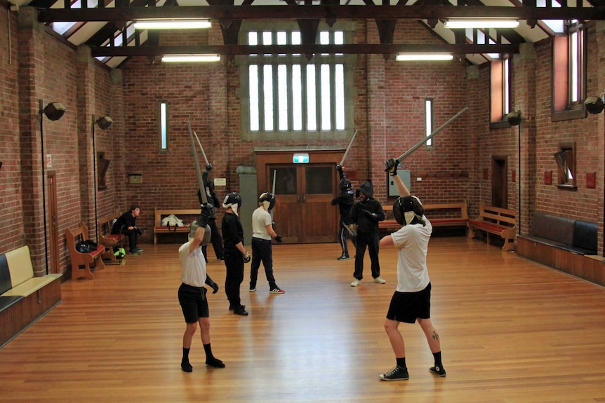 Students holding plastic swords over their heads in a church hall practicing sword fighting