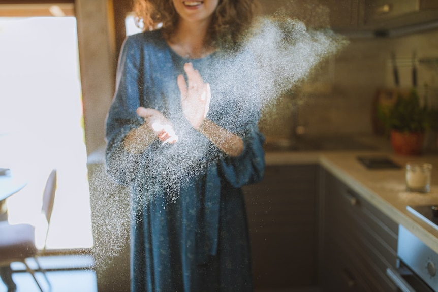 A woman in a blue dress holds her hands up in a cloud of dust, seen in a beam of sunlight