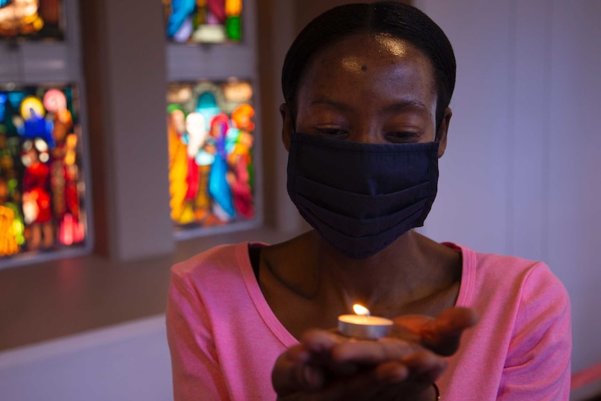 A woman wearing face mask holds a tea candle in a church.