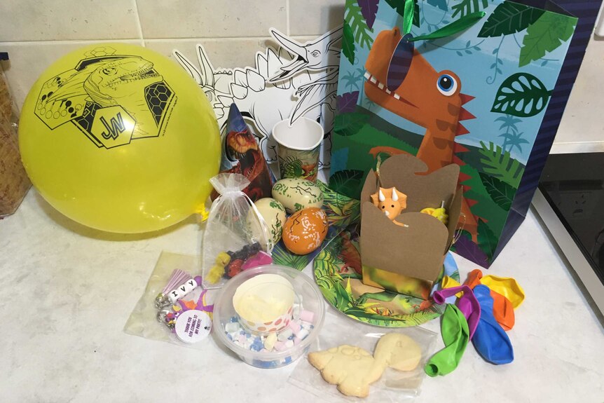 A dinosaur gift bag with other dinosaur party favours, yellow balloon and cookie.