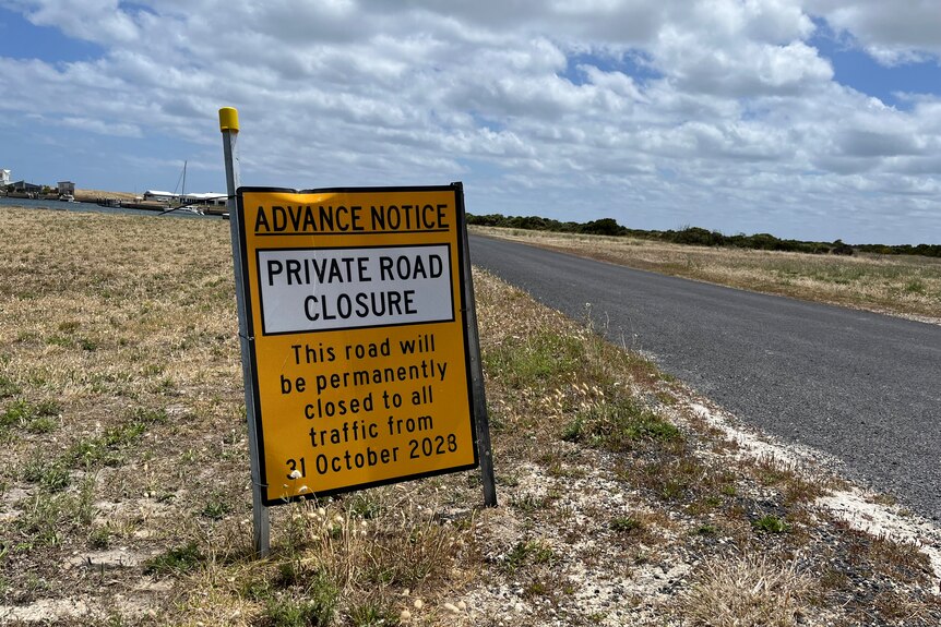 A sign saying PRIVATE ROAD CLOSURE on a road with dry grass on the side
