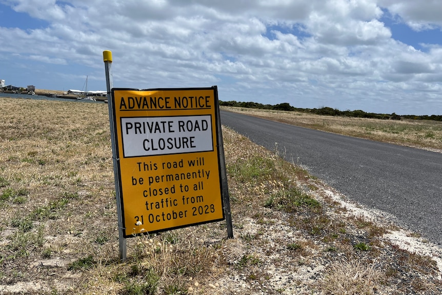A sign saying PRIVATE ROAD CLOSURE on a road with dry grass on the side