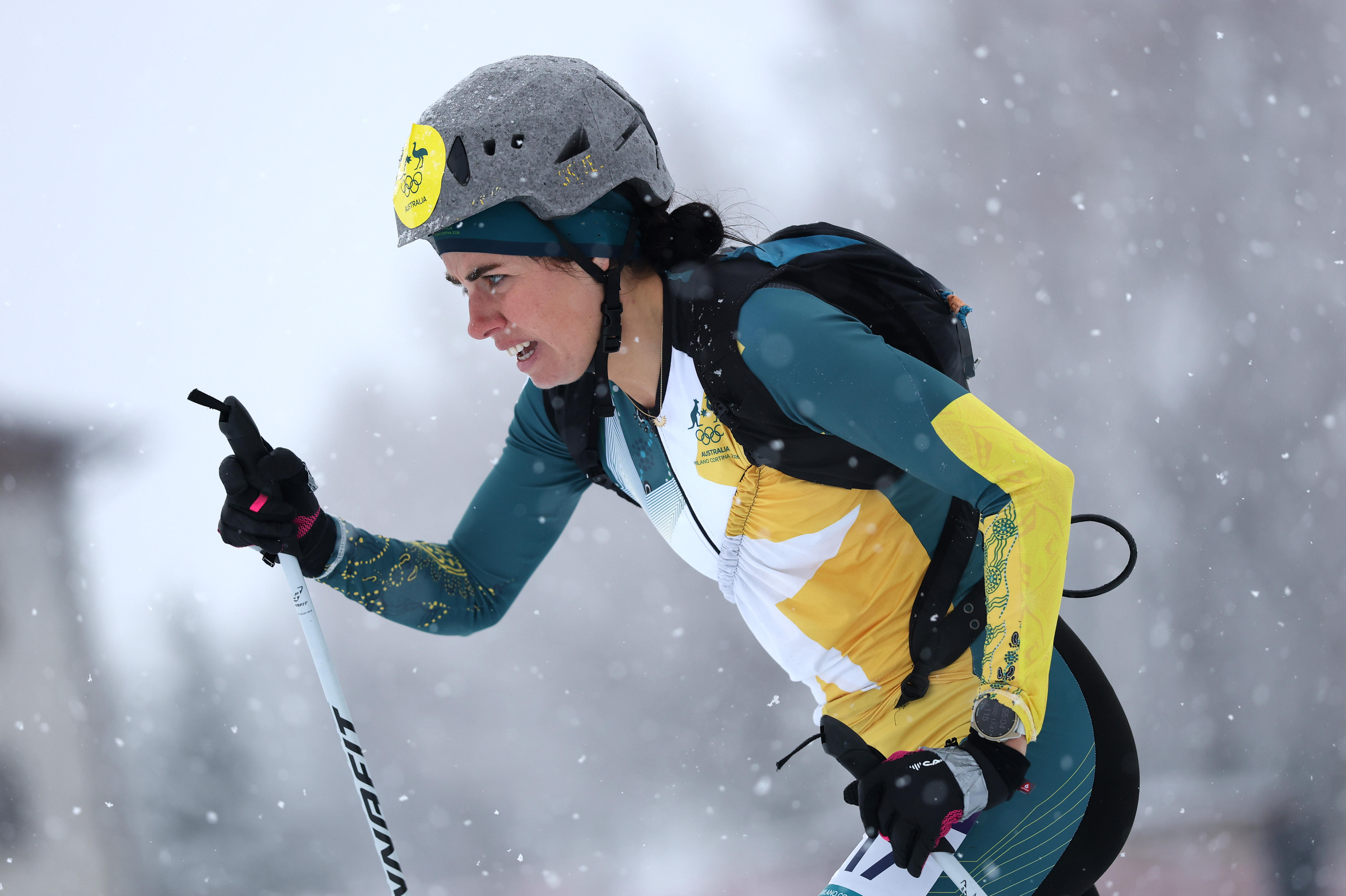 Um esquiador vestindo verde e dourado parece determinado na neve
