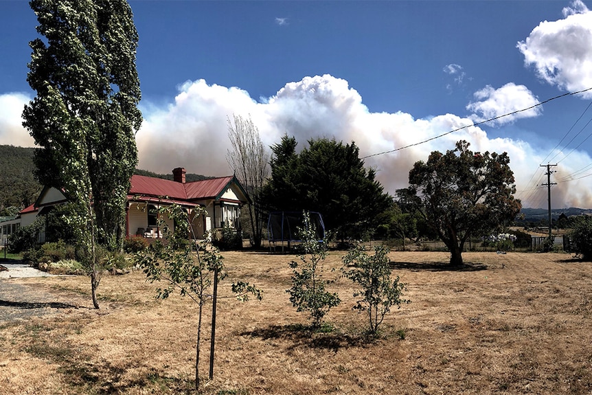 Old weatherboard cottage with clouds of smoke billowing in sky above.