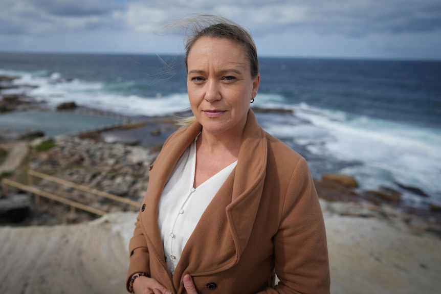 Woman looks solemn while standing at beach.